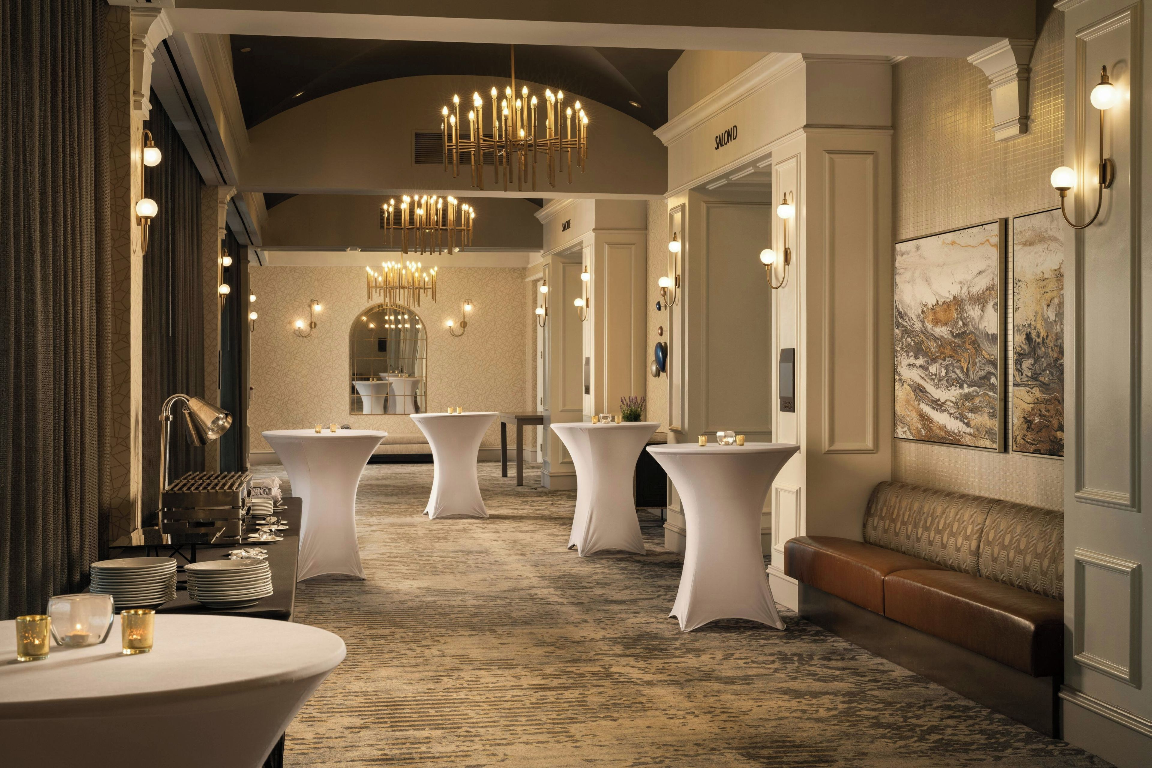 A hotel lobby with a grand chandelier, round tables, a reception desk, and a seating area.