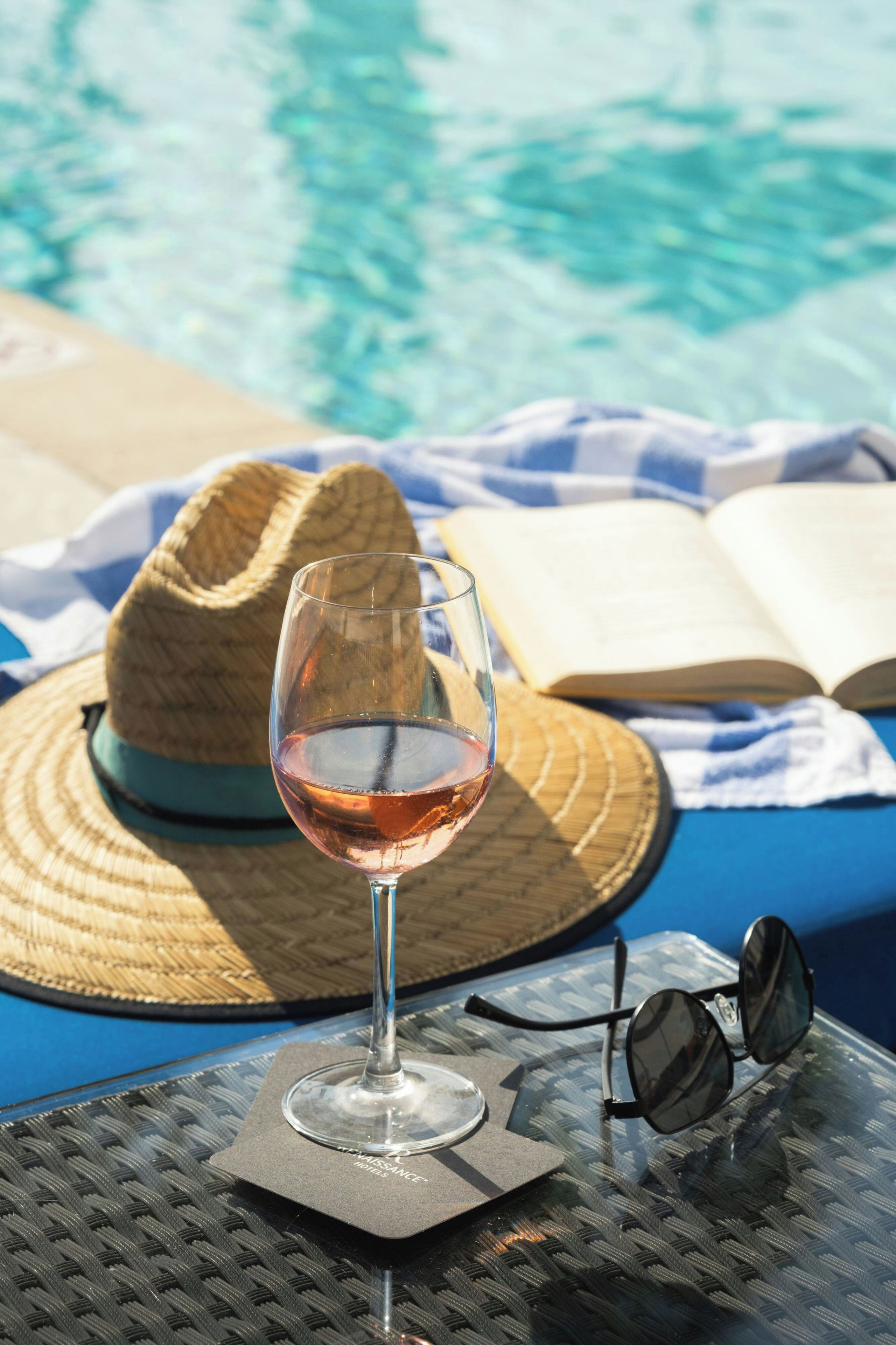Ein Weinglas, ein Strohhut und eine Sonnenbrille auf einem Tisch am Pool.