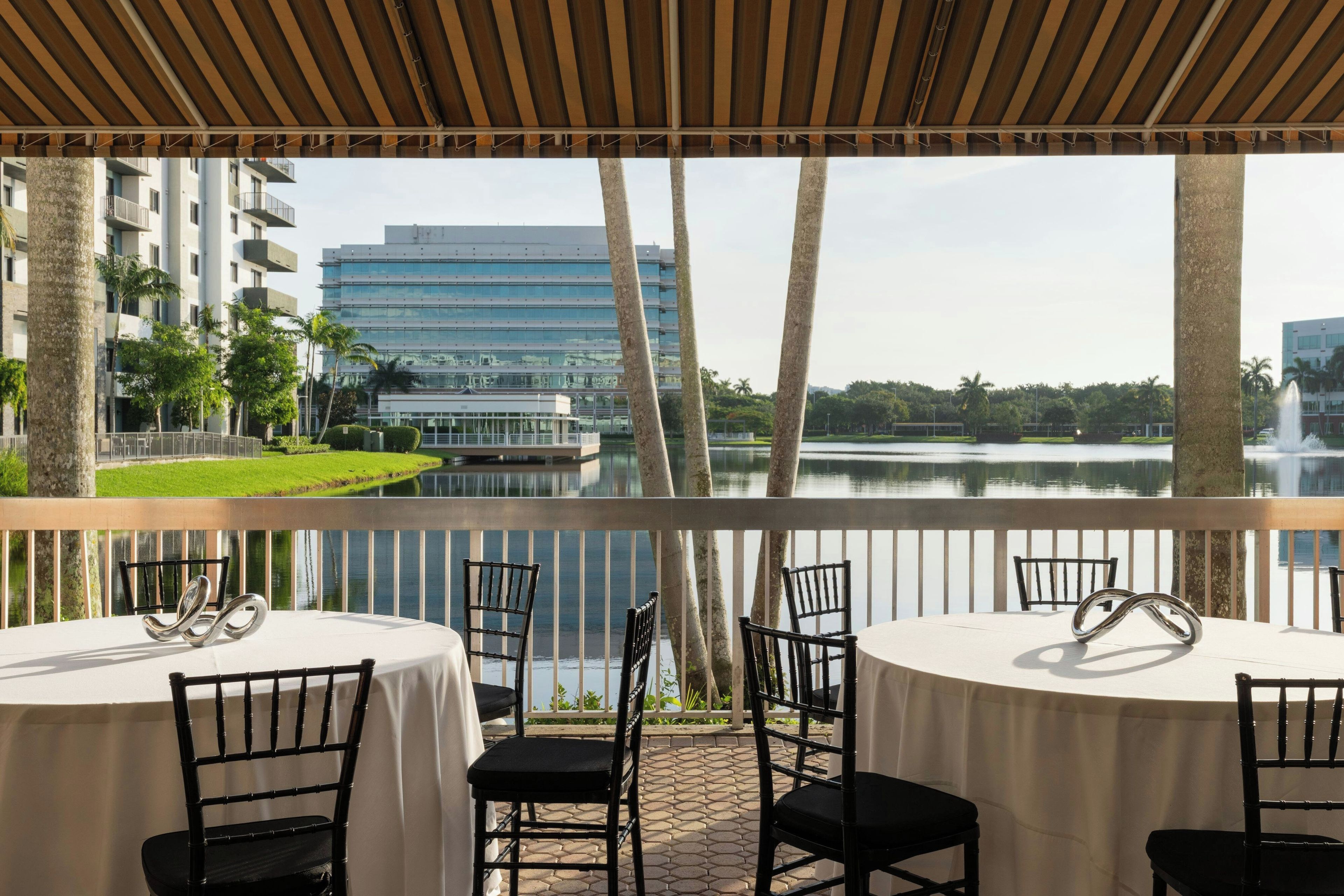 Une terrasse avec des tables et des chaises donnant sur un plan d’eau et des bâtiments.