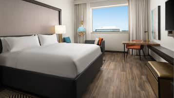 Habitación de hotel con una cama grande, un escritorio, una silla, un televisor y una ventana con vista a un edificio.