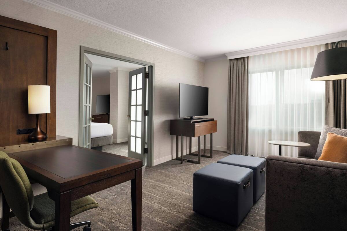 A hotel room with a wooden desk, a chair, a sofa, a TV, and a small table.