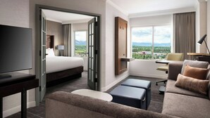 A hotel room with a bed, a sofa, a desk, and a TV. There is a large window with a view of mountains and a city. - Renaissance Boulder FlatIron Hotel (Broomfield)
