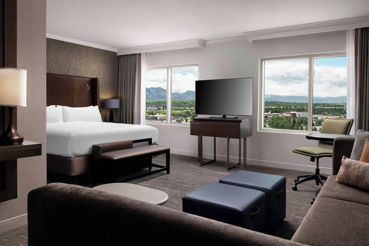 A hotel room with a large bed, a TV, a desk, and a view of mountains.
