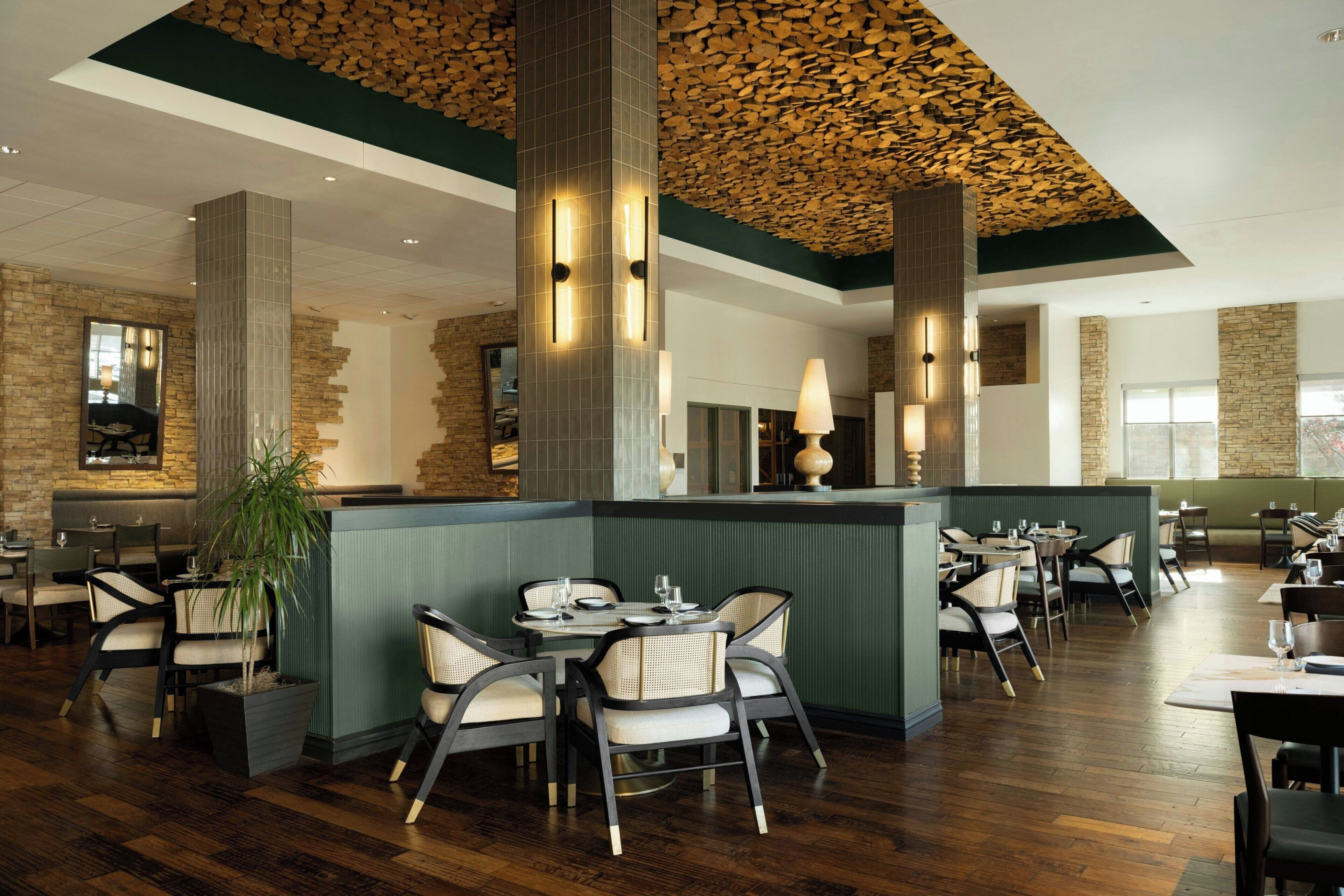 Un restaurant avec un plafond en bois, des murs en pierre et un espace avec des banquettes vertes.