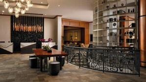 A modern lobby with a wooden reception desk, a seating area with a curved bench, a decorative light fixture, and a metal railing. - Renaissance Boulder FlatIron Hotel (Broomfield)