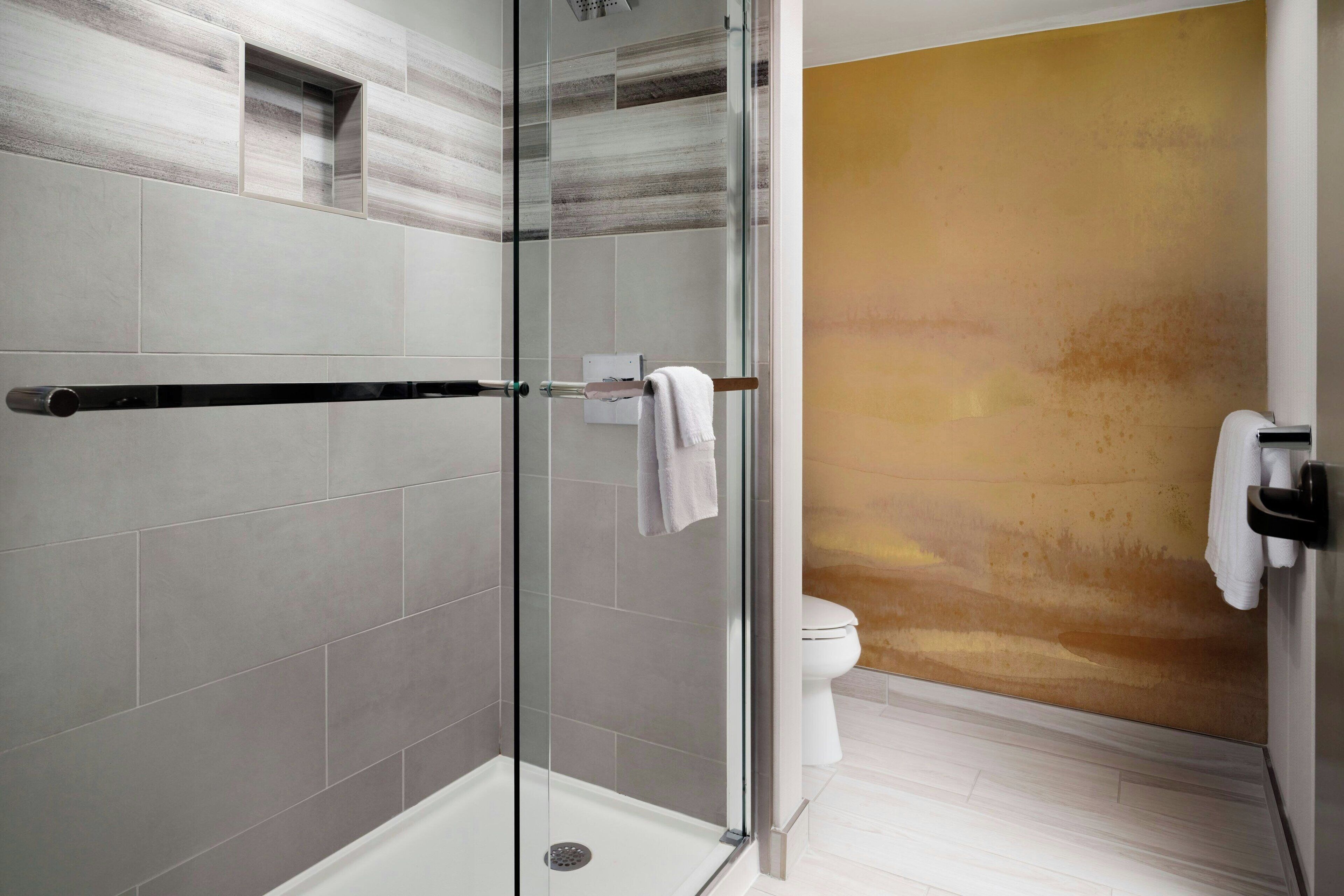 A modern bathroom with a glass shower enclosure, a white toilet, and a beige accent wall.