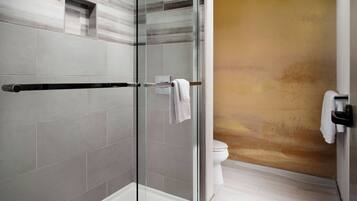 A modern bathroom with a glass shower enclosure, a white toilet, and a beige accent wall.