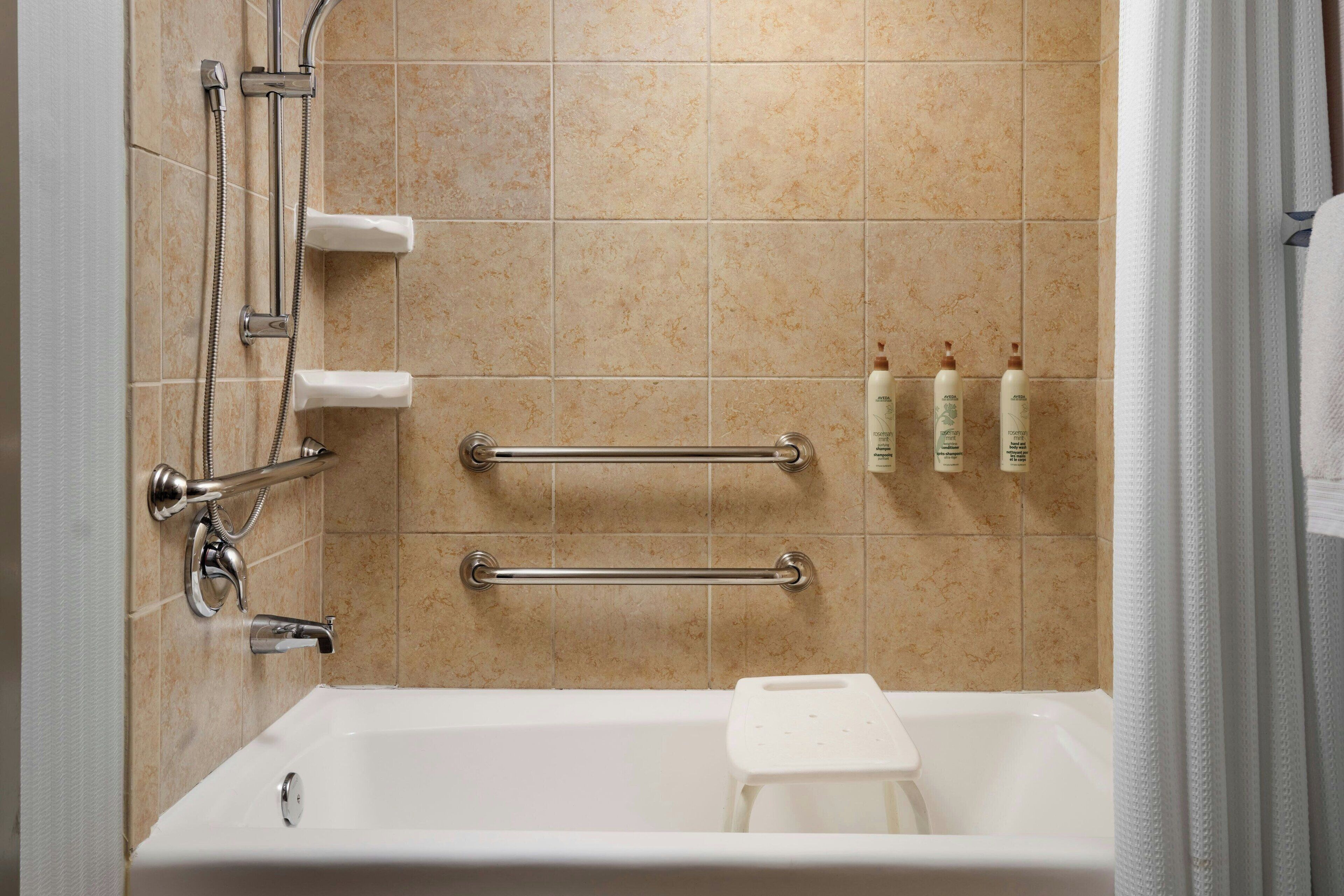 Une salle de bain équipée d’une baignoire, de barres d’appui, d’un pommeau de douche et d’un présentoir mural pour les articles de toilette.