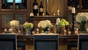 A dining area with a long table set for six, surrounded by chairs. There are wine bottles and a vase with flowers on the table. - Renaissance Boulder FlatIron Hotel (Broomfield)