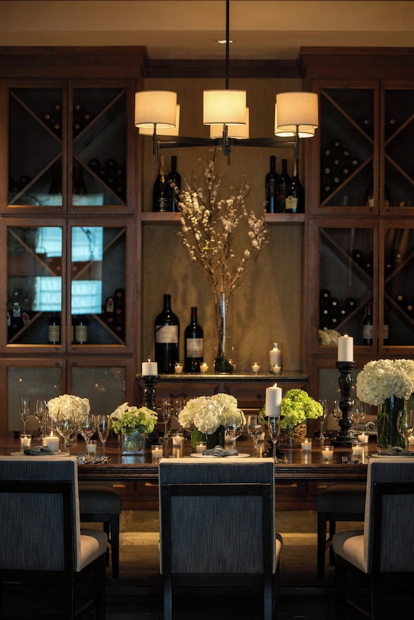 A dining area with a long table set for six, surrounded by chairs. There are wine bottles and a vase with flowers on the table. - Renaissance Boulder FlatIron Hotel (Broomfield)