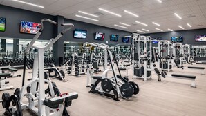 A gym with various exercise machines, mirrors, and TV screens displaying sports.