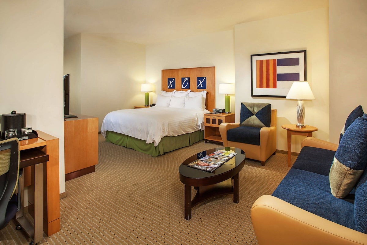 A hotel room with a bed, a desk, a chair, a sofa, and a coffee table.