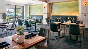 A modern dining area with tables set for dining, chairs, and potted plants.