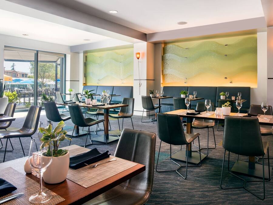 Un espace repas moderne, avec des tables dressées, des chaises et des plantes en pot.