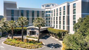 A modern hotel with a central courtyard, palm trees, and a clear sky.