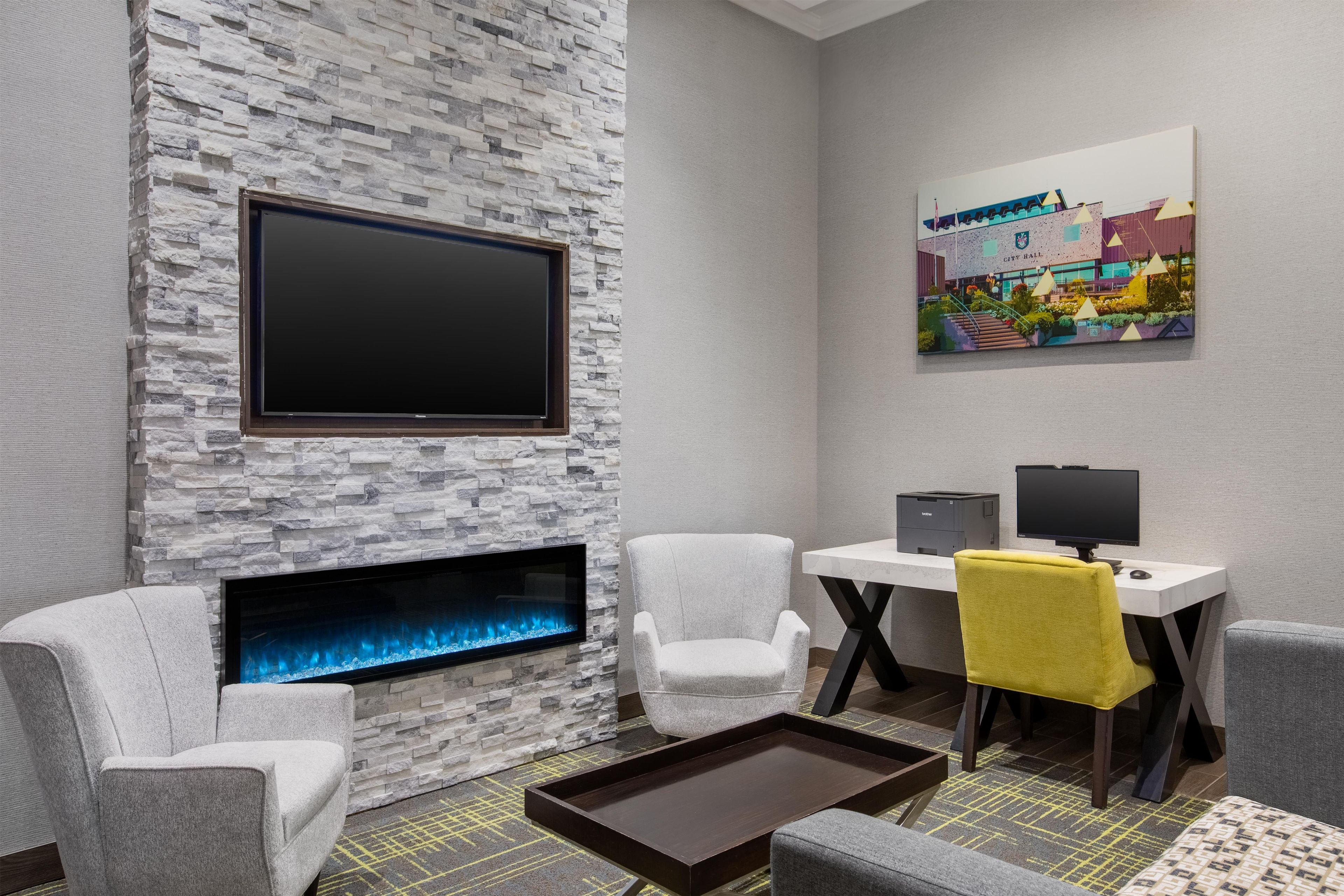 A modern room with a stone wall, a fireplace, a flat-screen TV, a desk with a computer, and a chair with a yellow cushion.