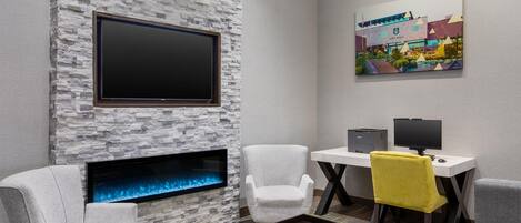 A modern room with a stone wall, a fireplace, a flat-screen TV, a desk with a computer, and a chair with a yellow cushion.