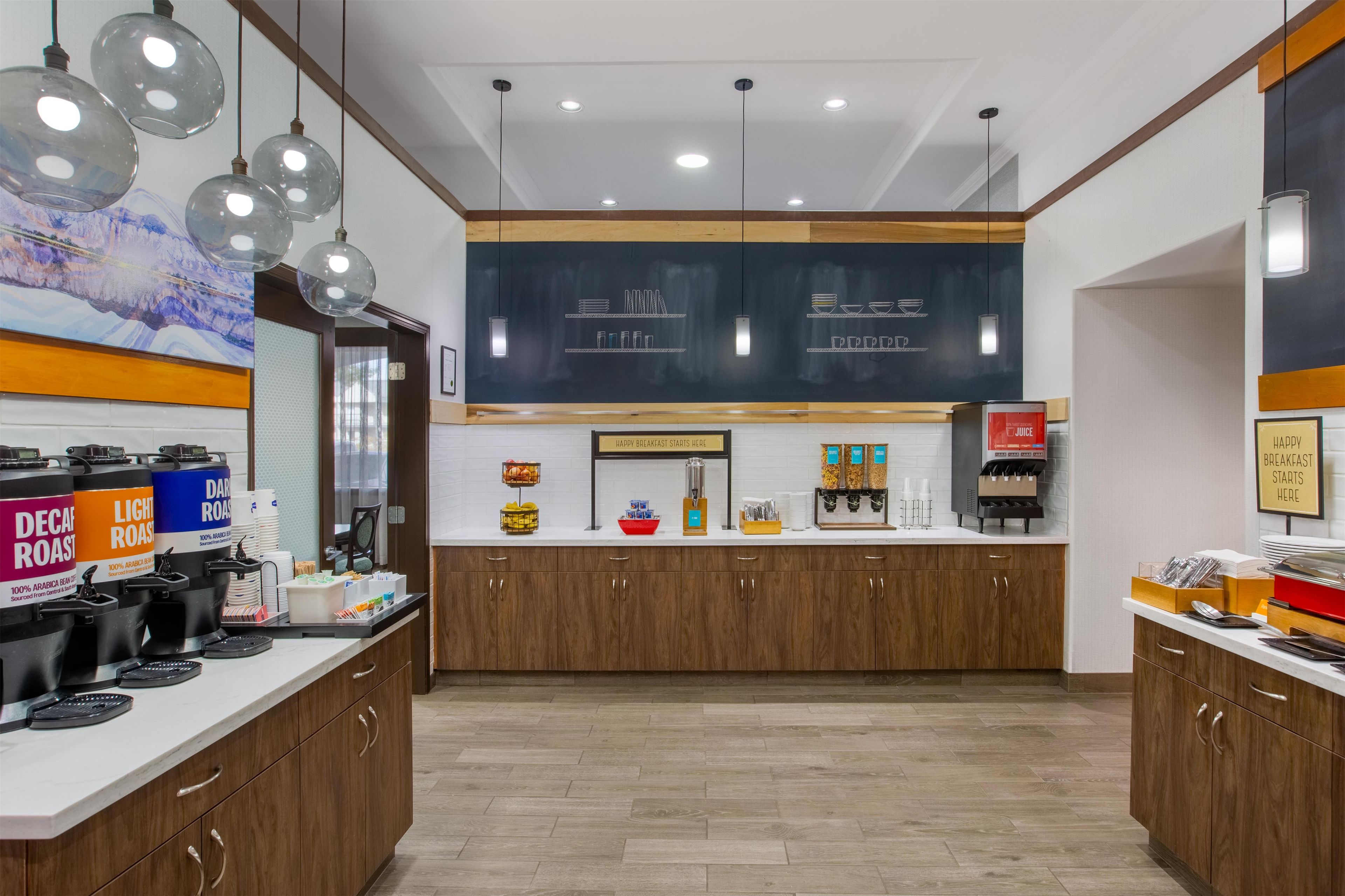 A breakfast area with a coffee machine, a juice dispenser, and a sign indicating breakfast starts here.