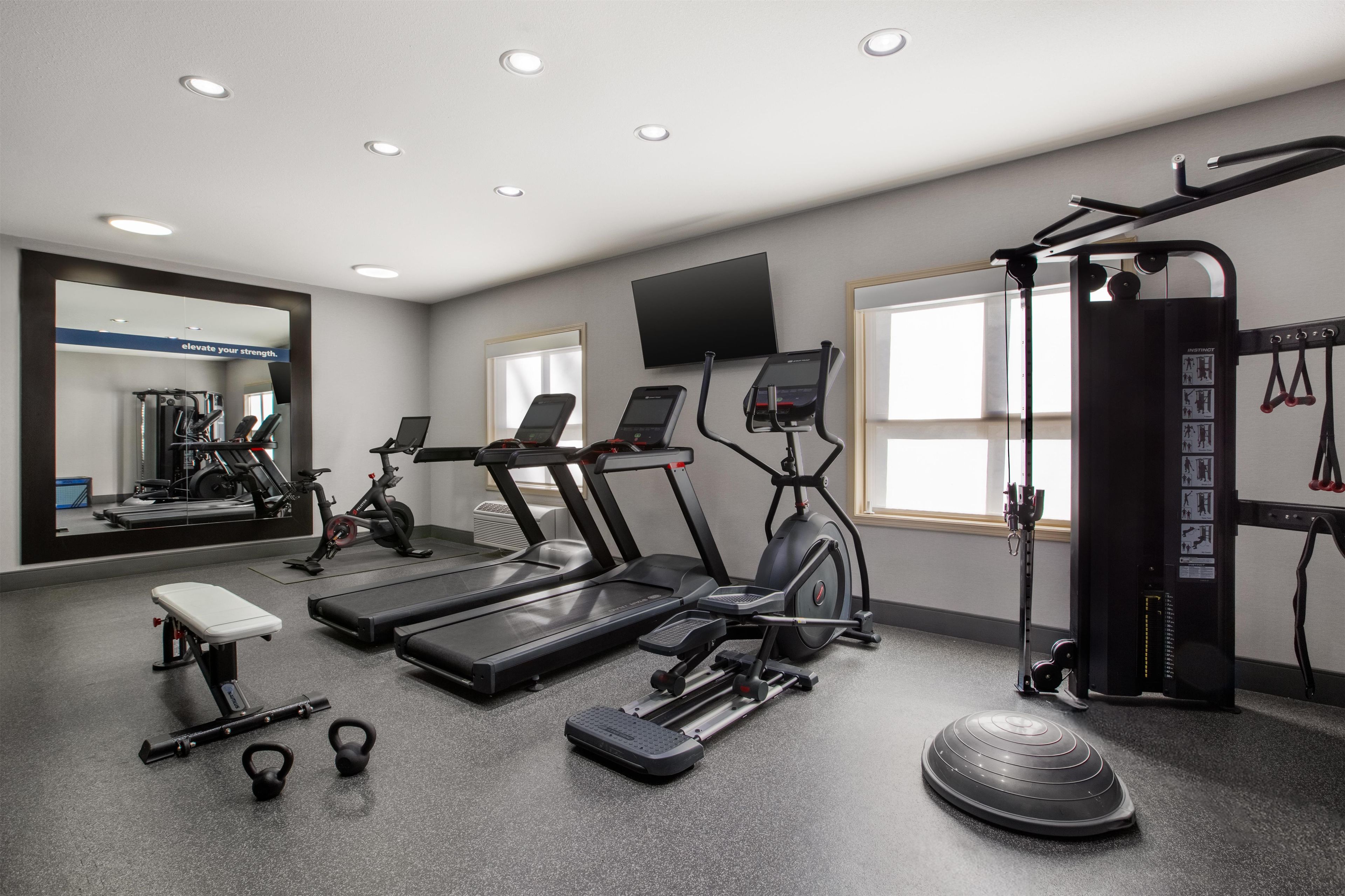 Une salle de sport équipée de tapis de course, d’un vélo elliptique, d’un banc de musculation, de kettlebells et d’une barre de traction.