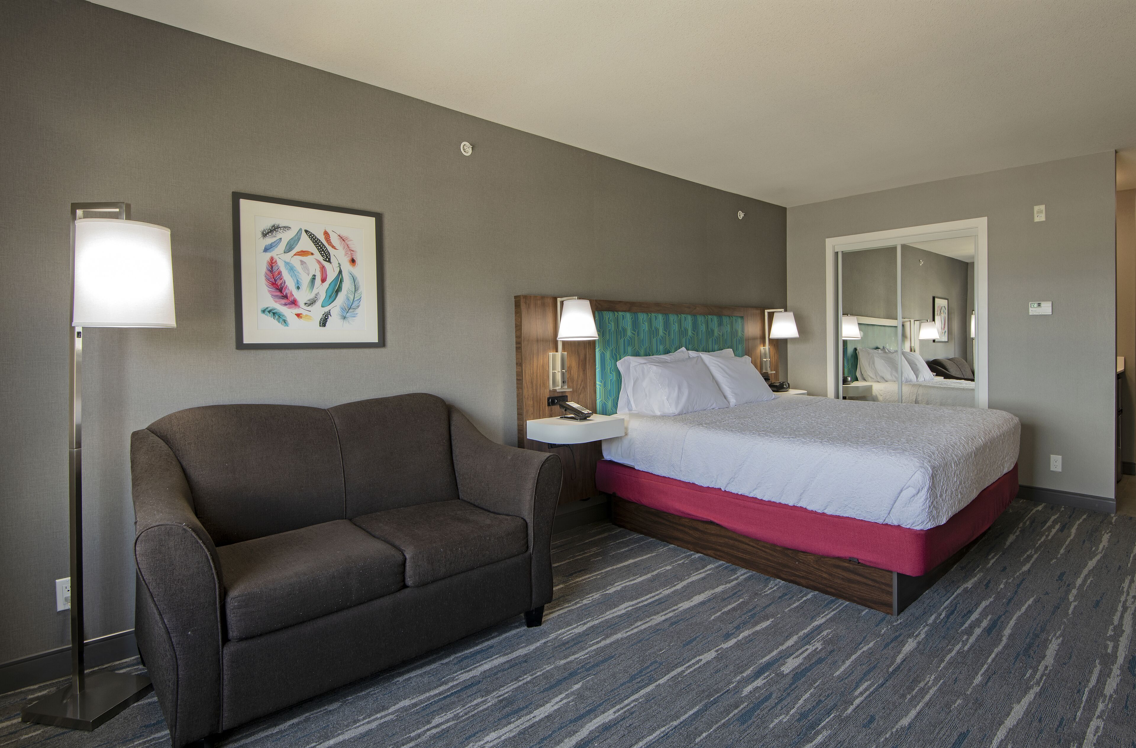 Una habitación de hotel con cama, sofá, mesita de noche y una lámpara de pared.