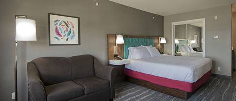 Una habitación de hotel con cama, sofá, mesita de noche y una lámpara de pared.