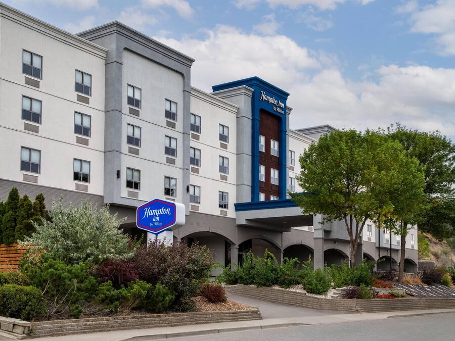 A Hampton Inn by Hilton hotel with a modern design, featuring multiple floors and a prominent blue and white color scheme.