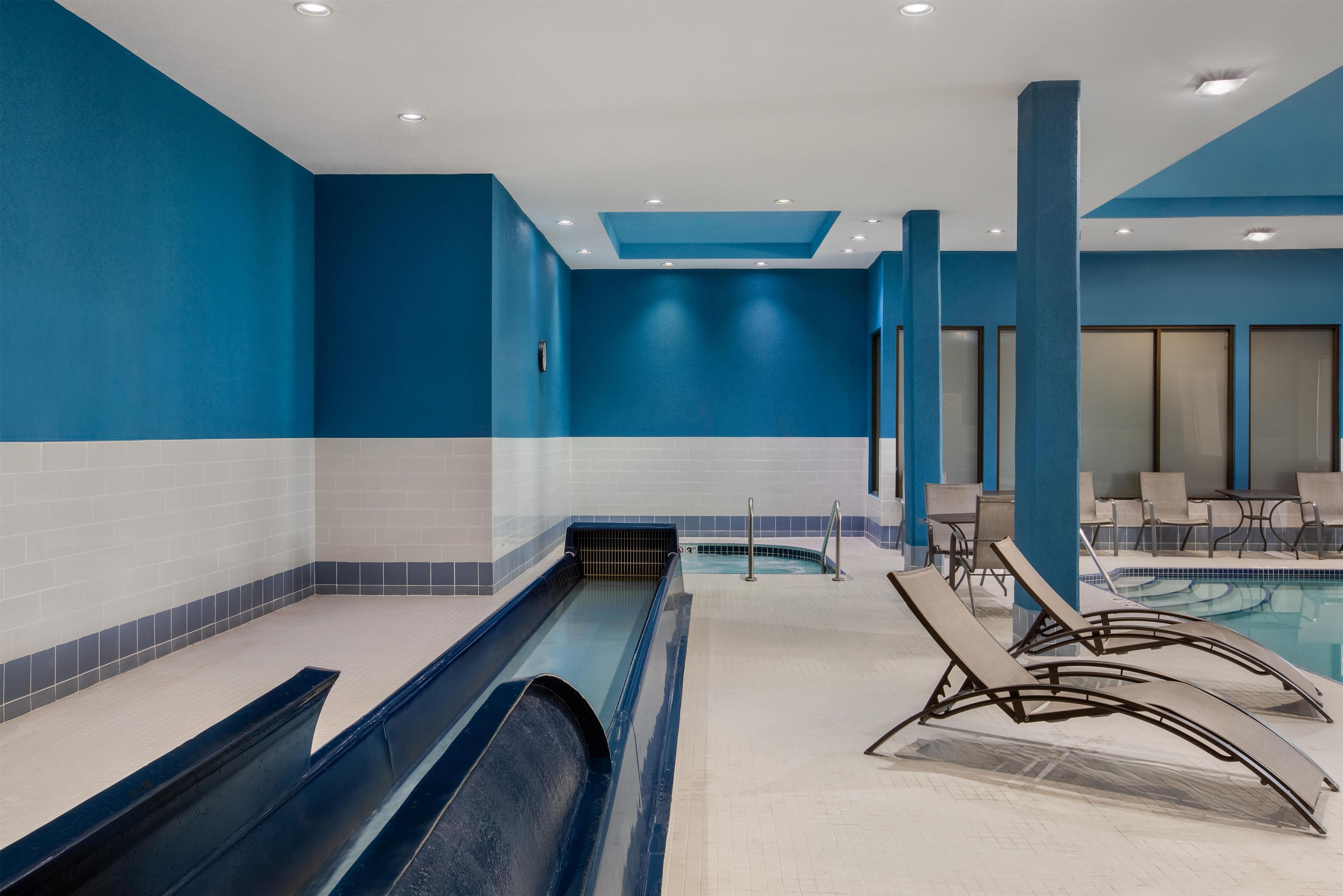 A swimming pool area with a water slide, lounge chairs, and a seating area with tables.