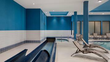 A swimming pool area with a water slide, lounge chairs, and a seating area with tables.