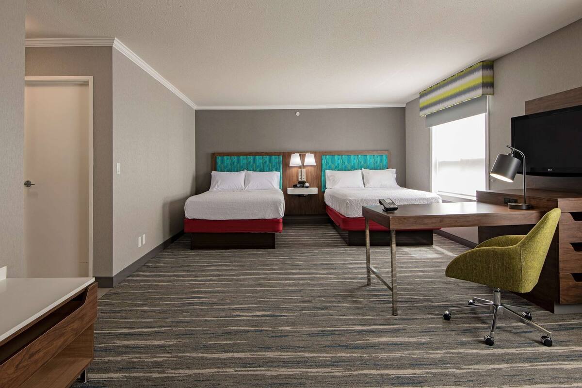 Habitación de hotel con dos camas, un escritorio, una silla, un televisor y una ventana.