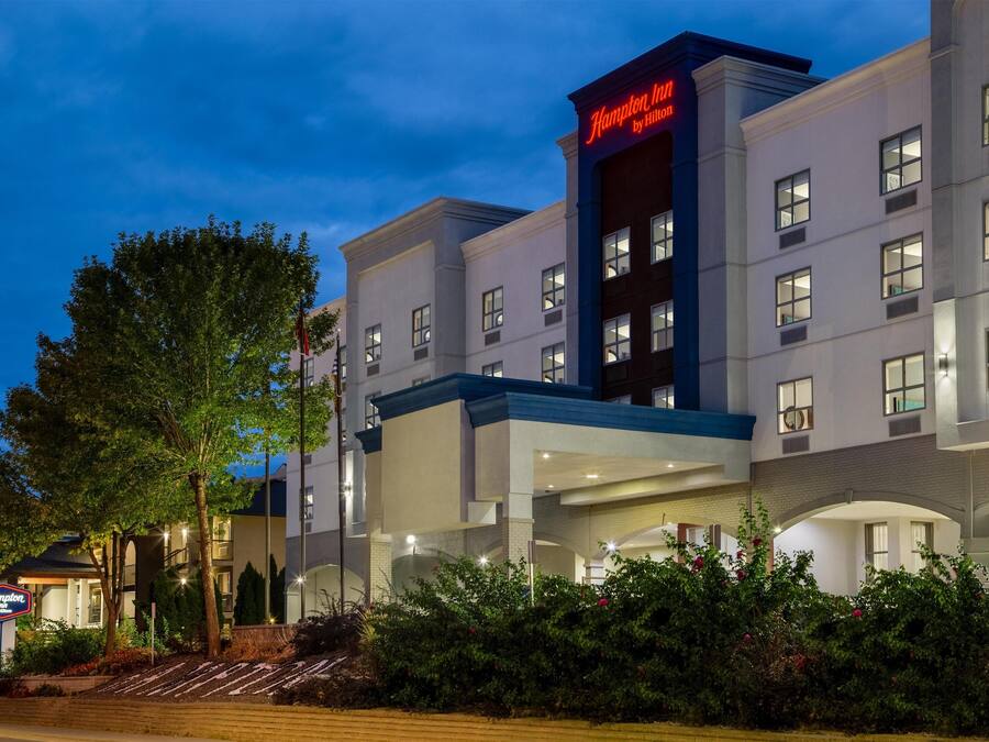 Un hotel Hampton Inn by Hilton con fachada moderna, varios pisos y una entrada bien iluminada.