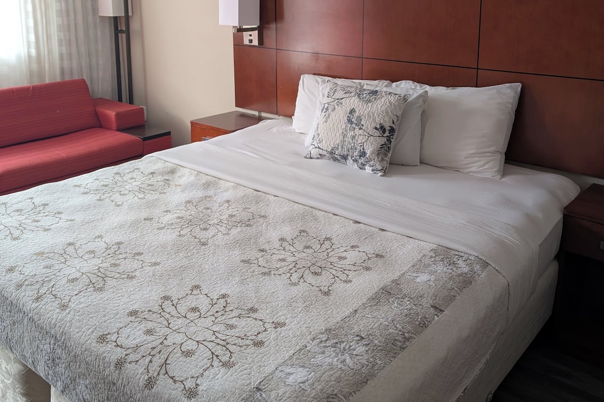 Ein Hotelzimmer mit einem großen Bett, einem roten Sofa, einem Nachttisch mit Lampe und einer Wand mit gerahmten Kunstwerken.