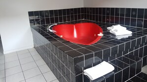 A modern bathroom with a heart-shaped bathtub, black and white tiles, and a white towel on the floor. - 7 Nights Stay (Niagara Falls)