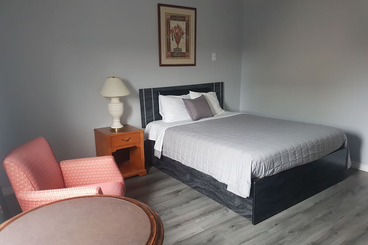 Ein Schlafzimmer mit Bett, Nachttisch, Lampe, Stuhl und einem gerahmten Bild an der Wand.