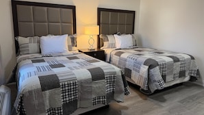 A hotel room with two beds, each with a quilted headboard, a bedside table with a lamp, and a wooden floor. - Knights Inn London (London)