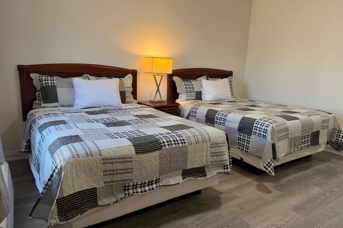 A double bed with a checkered quilt, a bedside table with a lamp, and a wooden floor.