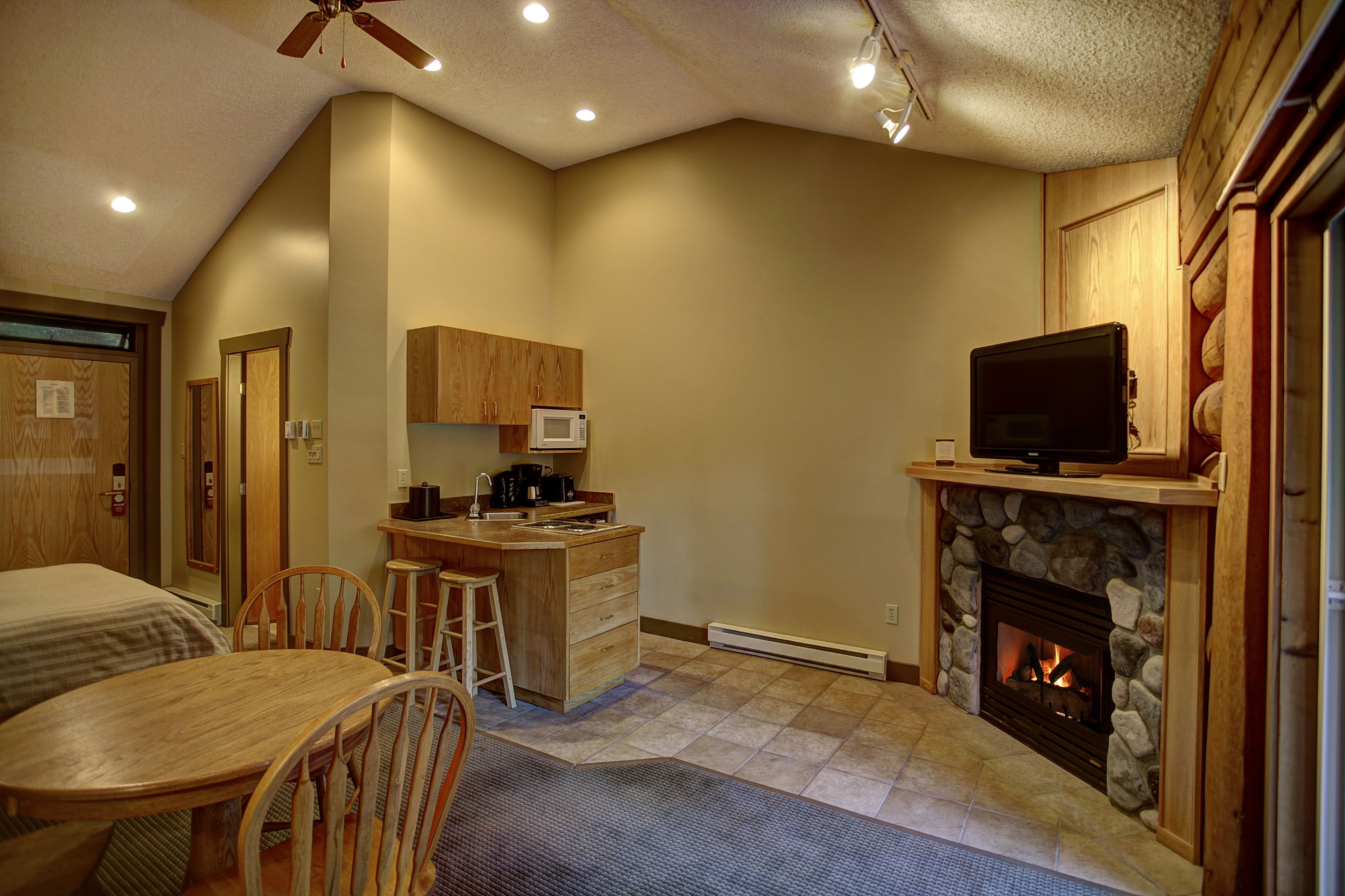 A cozy kitchen with wooden cabinets, a microwave, and a stone fireplace.