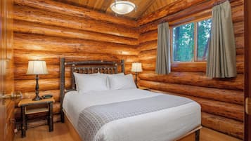 A log cabin bedroom with a wooden bed, two bedside lamps, and a window with curtains.
