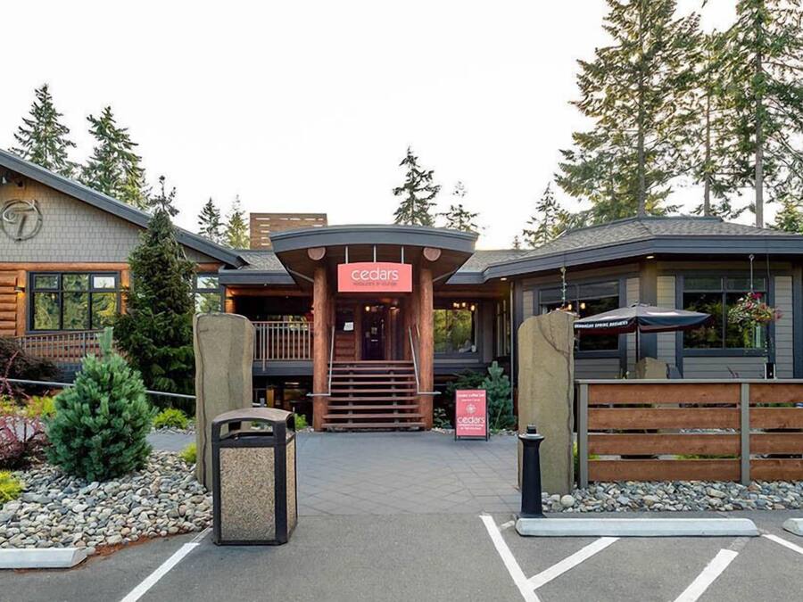Een lodge met een centrale ingang, houten gevel en een bordje met de tekst 'cedars'.