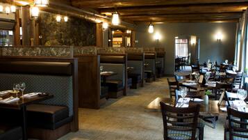 A restaurant with booths and tables, wooden beams on the ceiling, and stone walls.