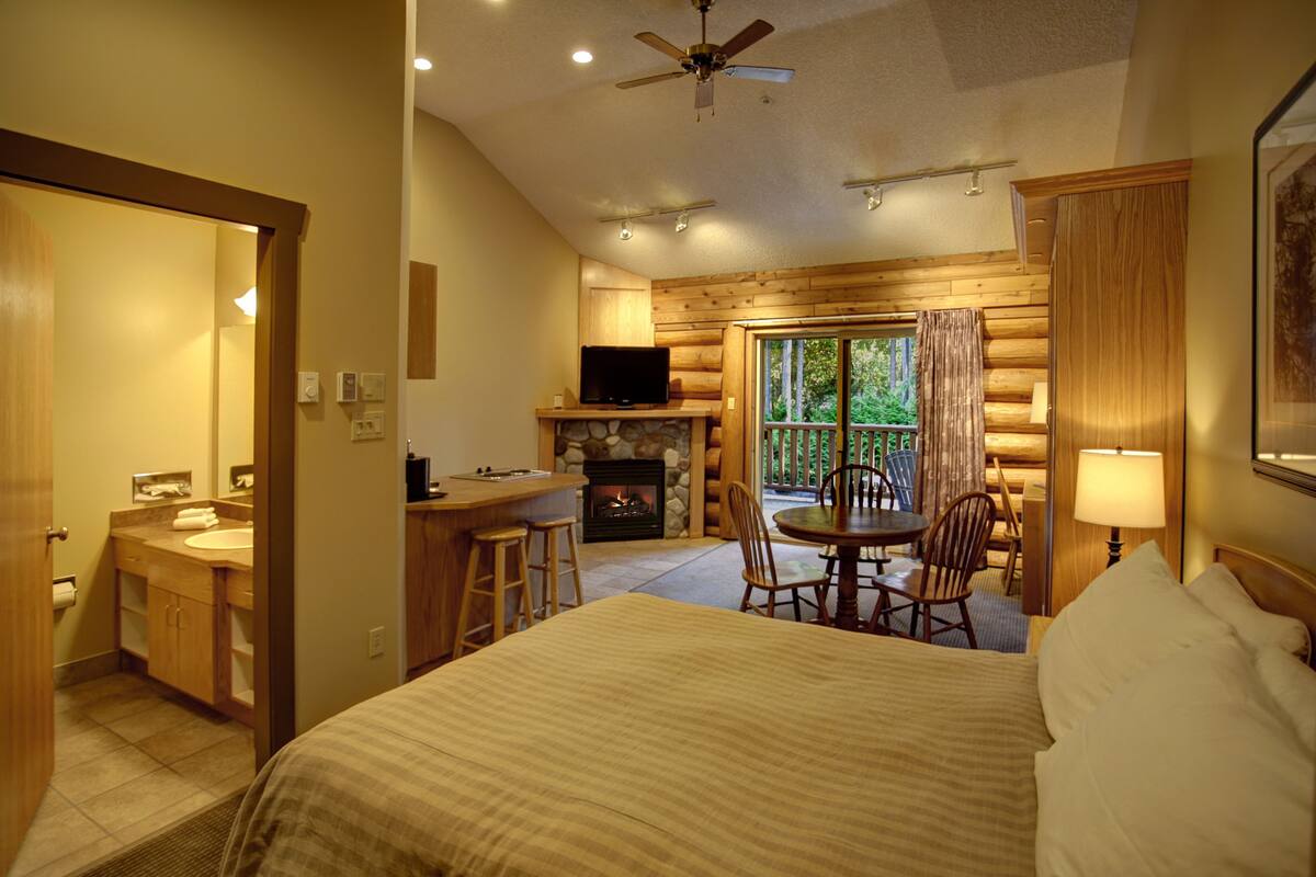 A hotel room with a bed, a desk with a television, a fireplace, and a balcony with chairs.