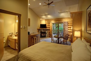 A hotel room with a bed, a desk with a television, a fireplace, and a balcony with chairs.