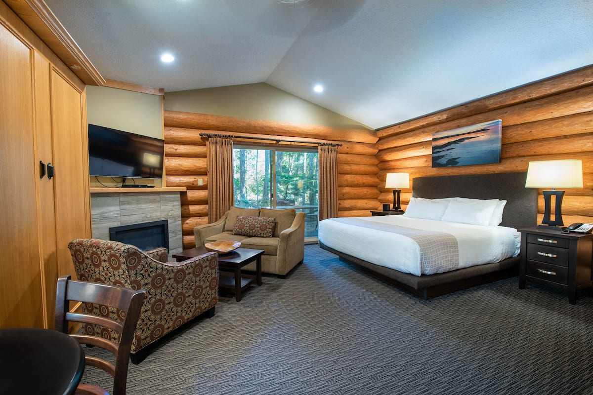 A log cabin-style room with a bed, a sofa, a chair, a TV, and a fireplace.