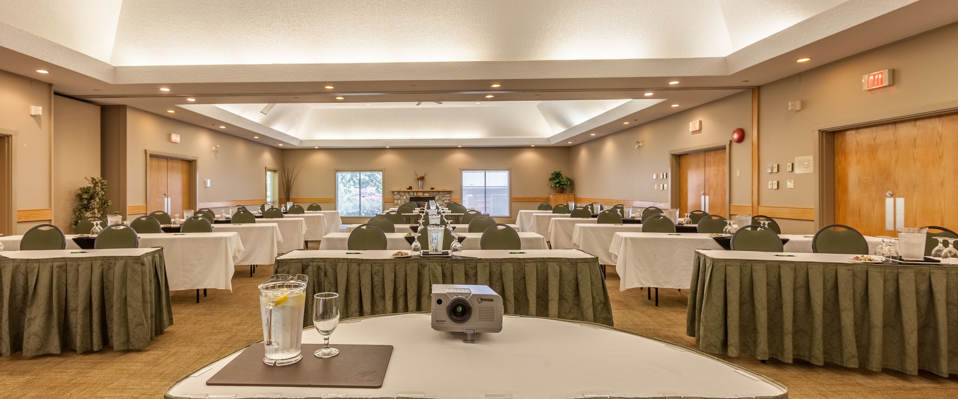 A conference room with multiple tables, chairs, a projector, and a water pitcher.