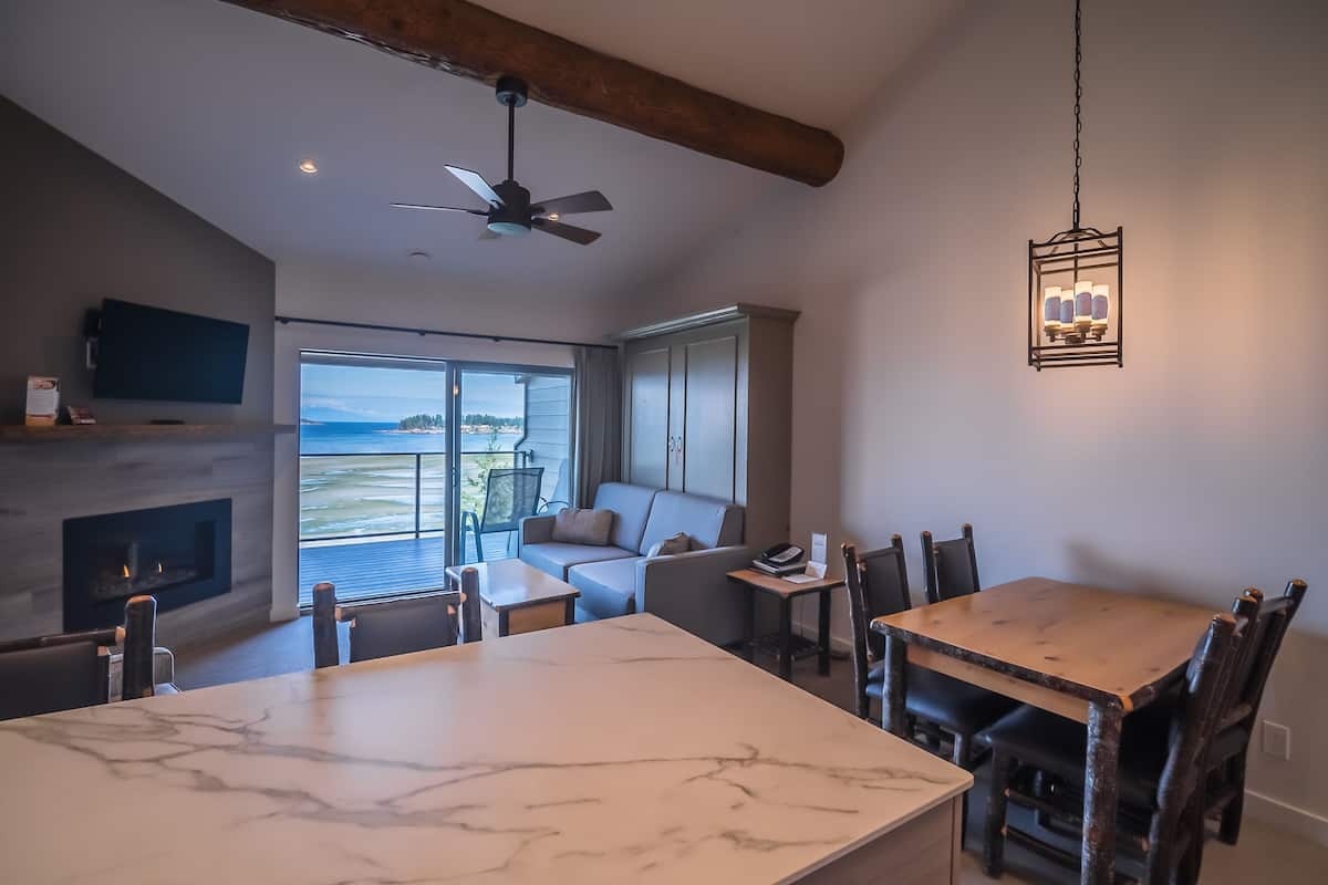 A modern living room with a fireplace, a dining table, and a large window offering a view of the outdoors.