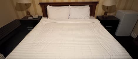 A neatly made bed in a hotel room with striped wallpaper, two bedside tables with lamps, and a framed picture on the wall.