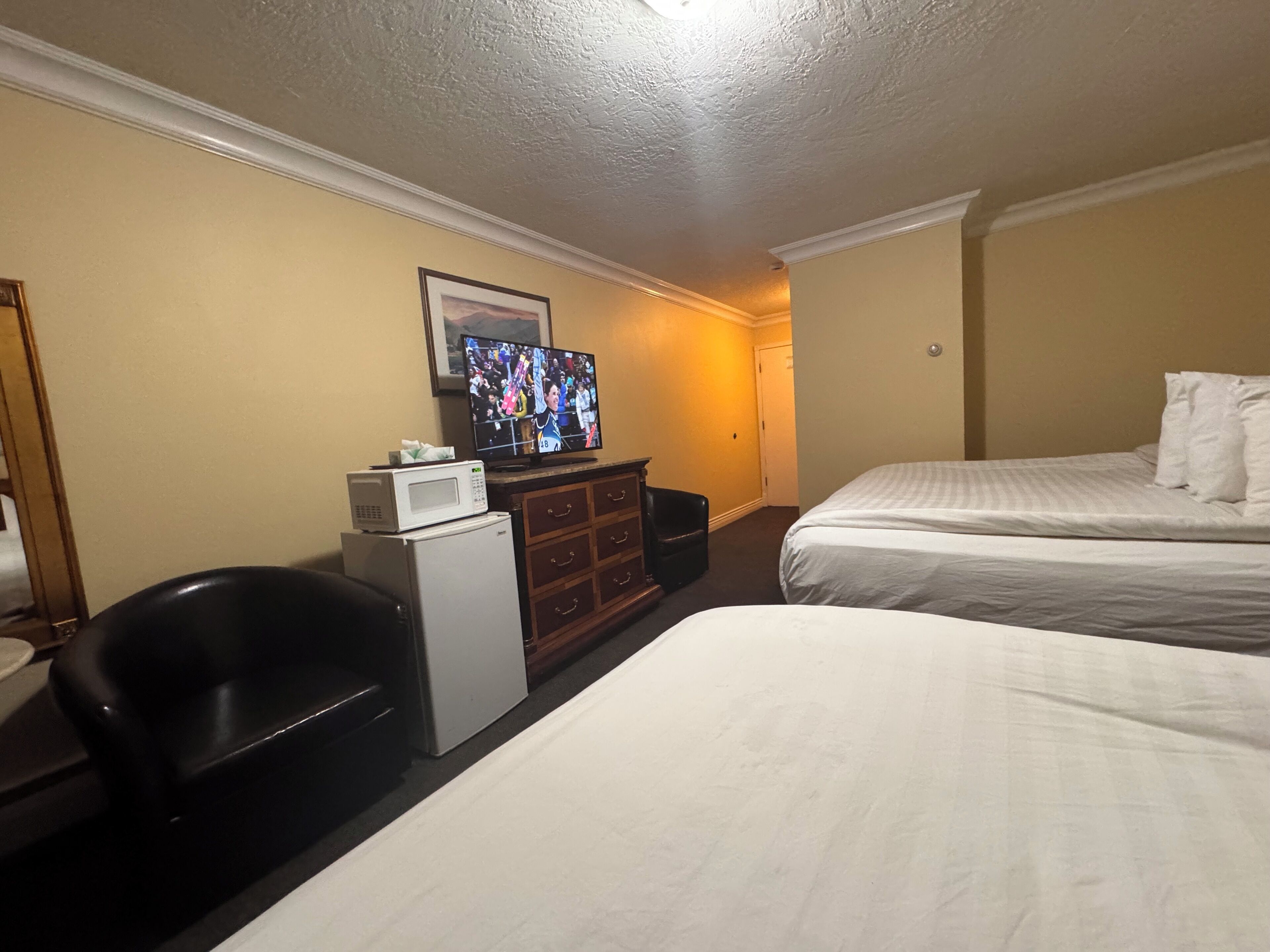 A hotel room with two beds, a TV, a microwave, a refrigerator, a desk, and a chair.