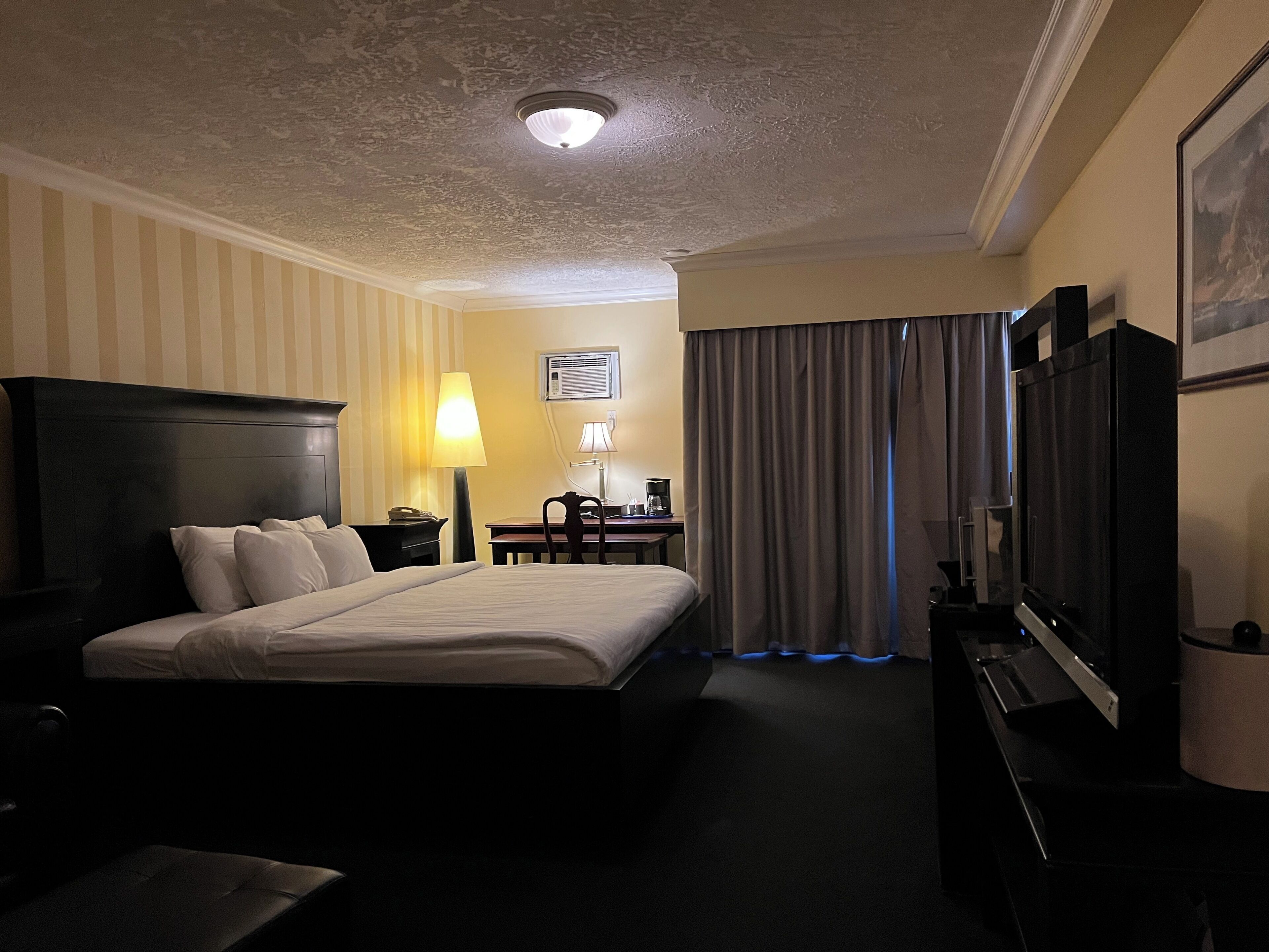 A hotel room with a large bed, a desk with a lamp, a TV, and a window with curtains.