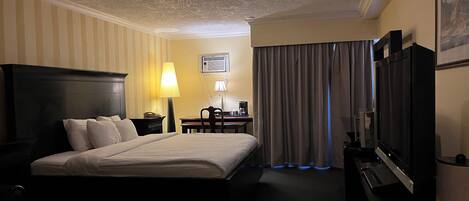 A hotel room with a large bed, a desk with a lamp, a TV, and a window with curtains.