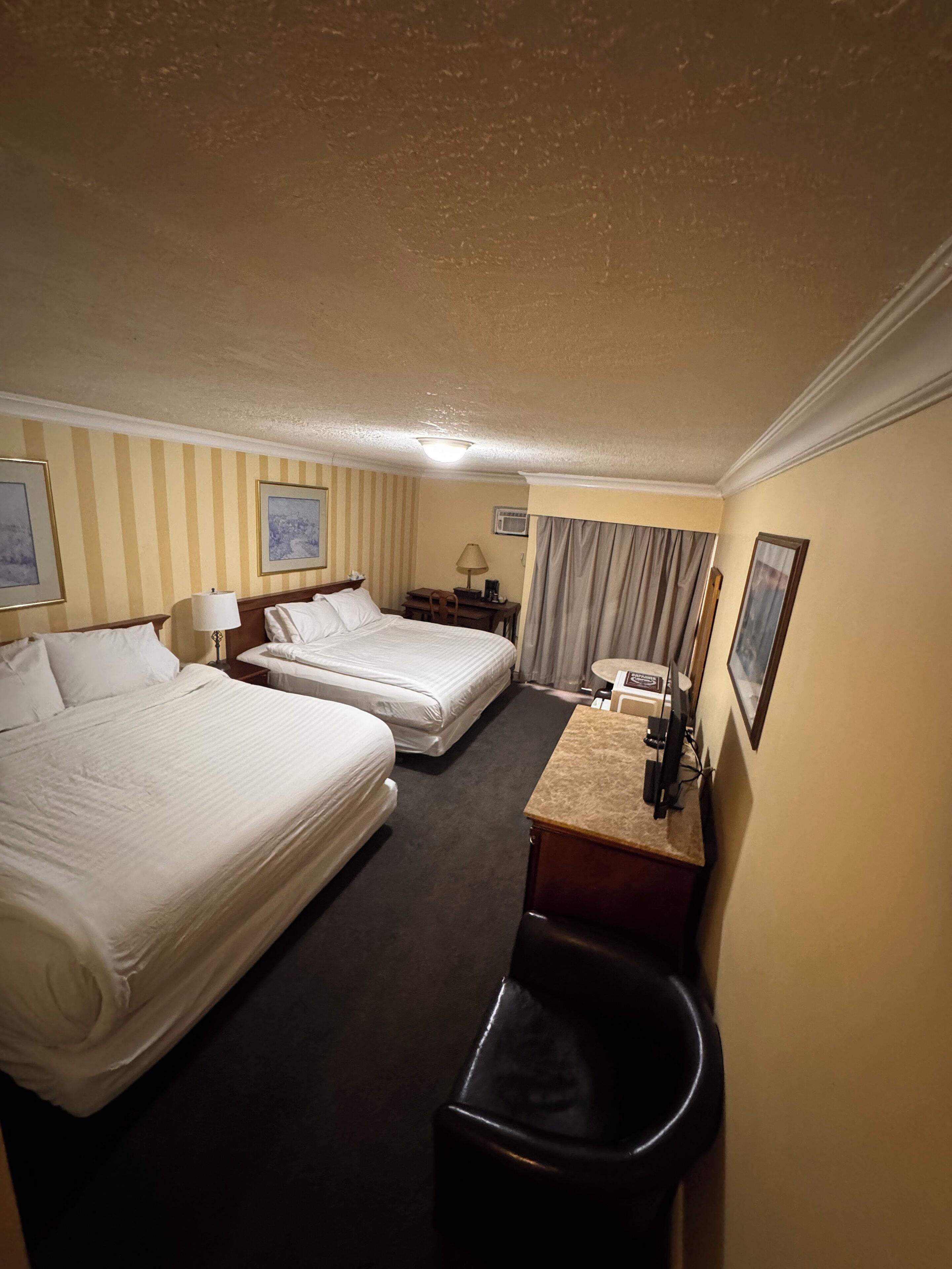 Een hotelkamer met twee bedden, een bureau met een computer, een stoel, een klein tafeltje met een lamp en een prullenbak.