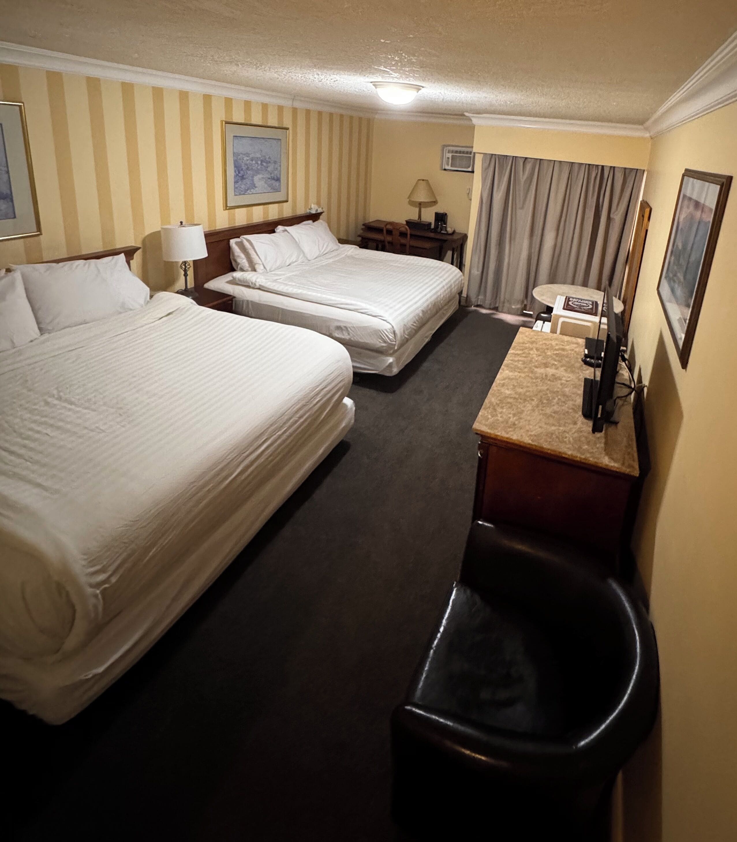 Ein Hotelzimmer mit zwei Betten, einem Schreibtisch mit Stuhl, einer Lampe und einem Fernseher.